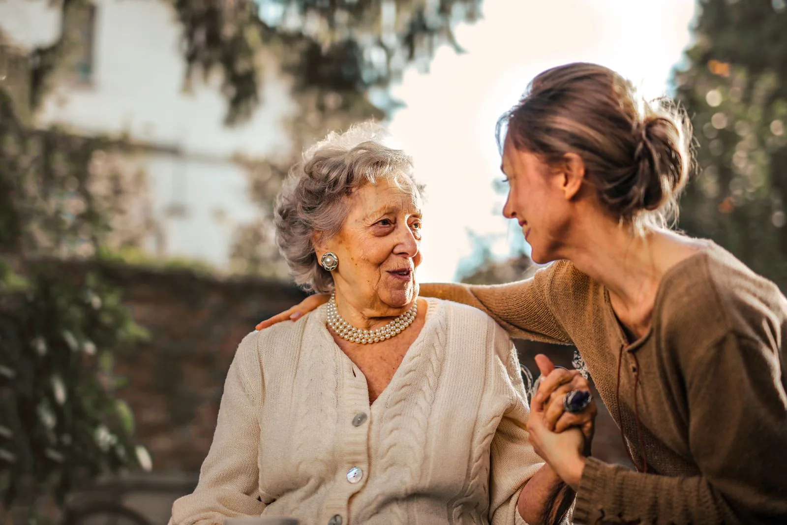 An adult daughter joyfully greeting her senior mother in a sunny garden